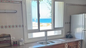 Une cuisine avec des meubles de rangement en bois, un évier et une fenêtre donnant sur une plage.