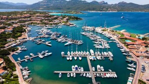 An aerial view of a marina with numerous boats docked, surrounded by residential buildings and mountains in the background. - Sunset Suite Sardinia 0.10 (Porto Rotondo)