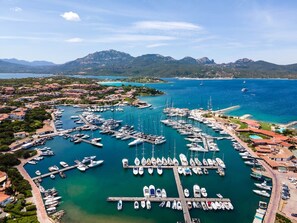 An aerial view of a marina with numerous boats docked, surrounded by residential buildings and mountains in the background.