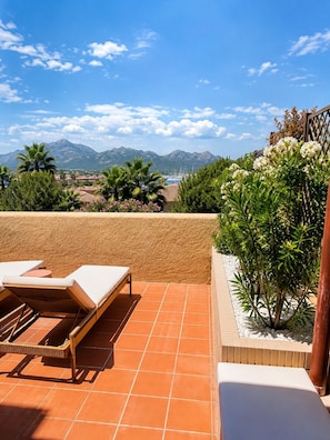 Une terrasse avec des chaises longues, une vue sur les montagnes et un plan d’eau.