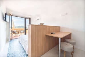 A modern hotel room with a bed, a small desk, and a view of the outdoors.