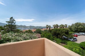 A balcony with a view of a marina, parked cars, and lush greenery. - Sunset Suite Sardinia 0.9 (Porto Rotondo)