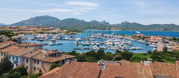 Marina con barcos amarrados, rodeada de edificios residenciales y montañas al fondo.