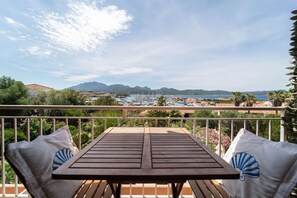 A wooden table with two white pillows, a balcony railing, and a scenic view of a marina and mountains.
