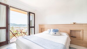 Une chambre d’hôtel avec un grand lit, une tête de lit en bois et une vue sur la mer, visible par une porte ouverte.