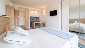 Une chambre d’hôtel moderne dotée d’un grand lit, d’une petite kitchenette, d’un téléviseur fixé au mur et d’un placard à portes coulissantes.