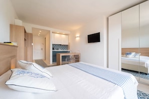 A modern hotel room with a large bed, a small kitchenette, a TV mounted on the wall, and a sliding door closet.