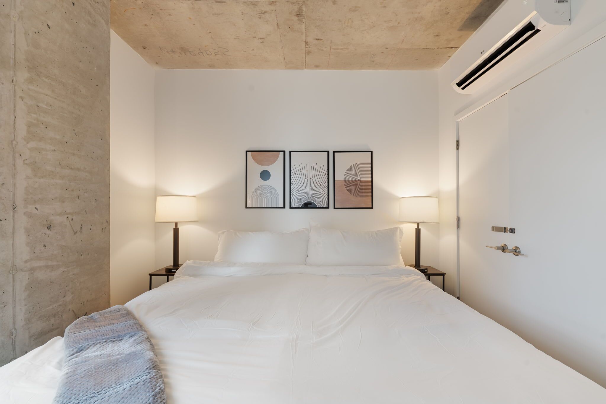 A bedroom with a large bed, two bedside lamps, and three framed artworks on the wall.