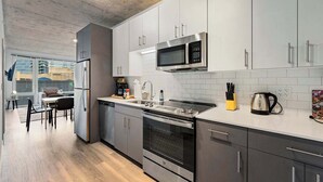 A modern kitchen with stainless steel appliances, grey cabinets, and a white countertop.