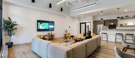 A modern office space with a large sofa, a small table, and a TV screen displaying a presentation.