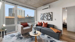 A modern living room with a large window, a grey sofa, a beige armchair, and a round coffee table.