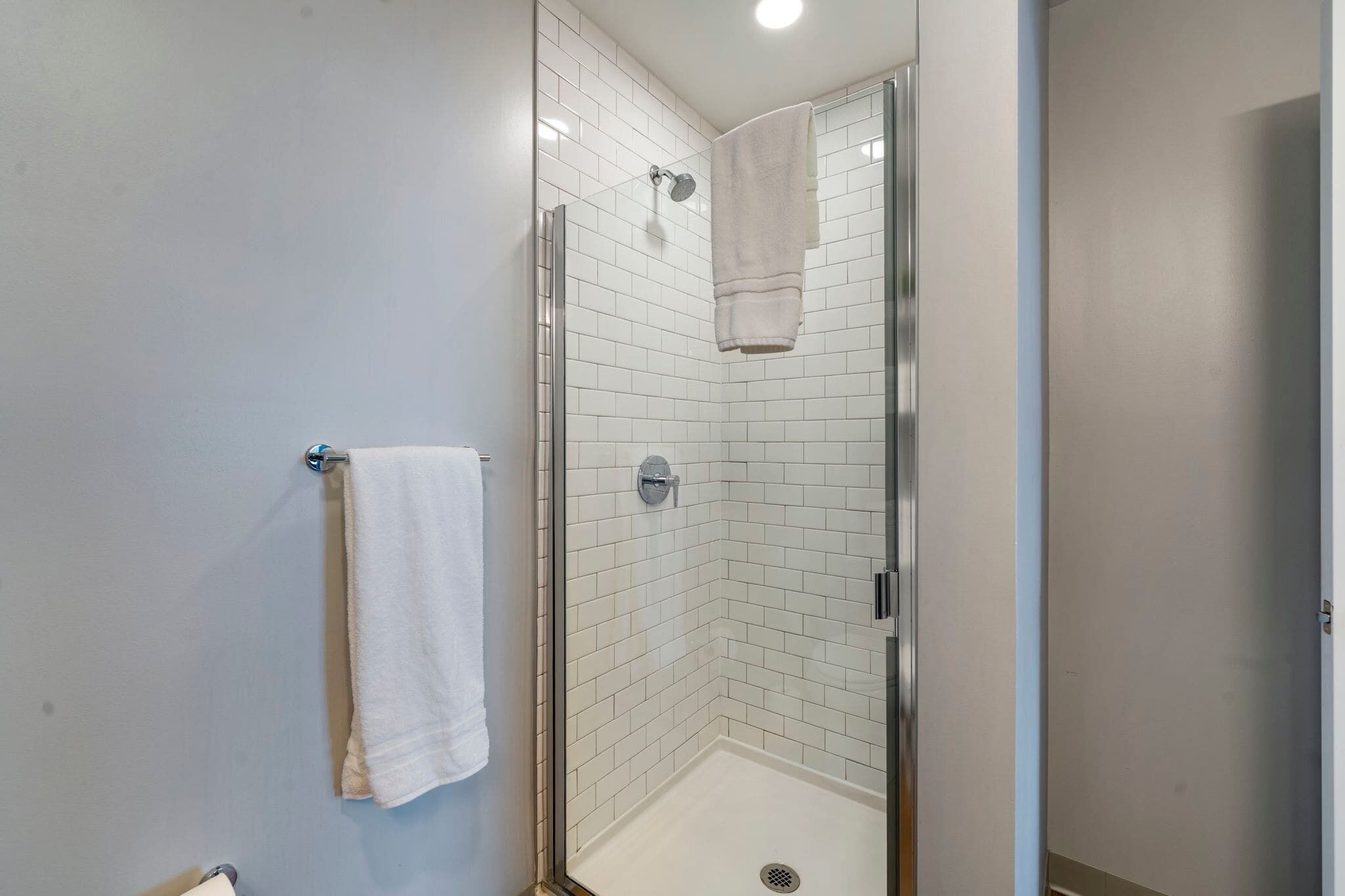 Een moderne badkamer met een douchecabine van glas, witte betegelde wanden en een witte handdoek aan de muur.