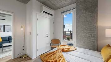 Een moderne slaapkamer met een groot bed, stadszicht en een wand van beton.