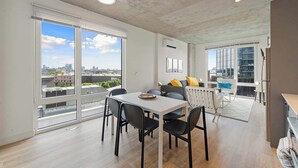 A modern apartment with a dining area, a living space with a sofa and cushions, and large windows offering city views. - Modern 2BR Retreat Near Old Town & Lincoln Park (Chicago)