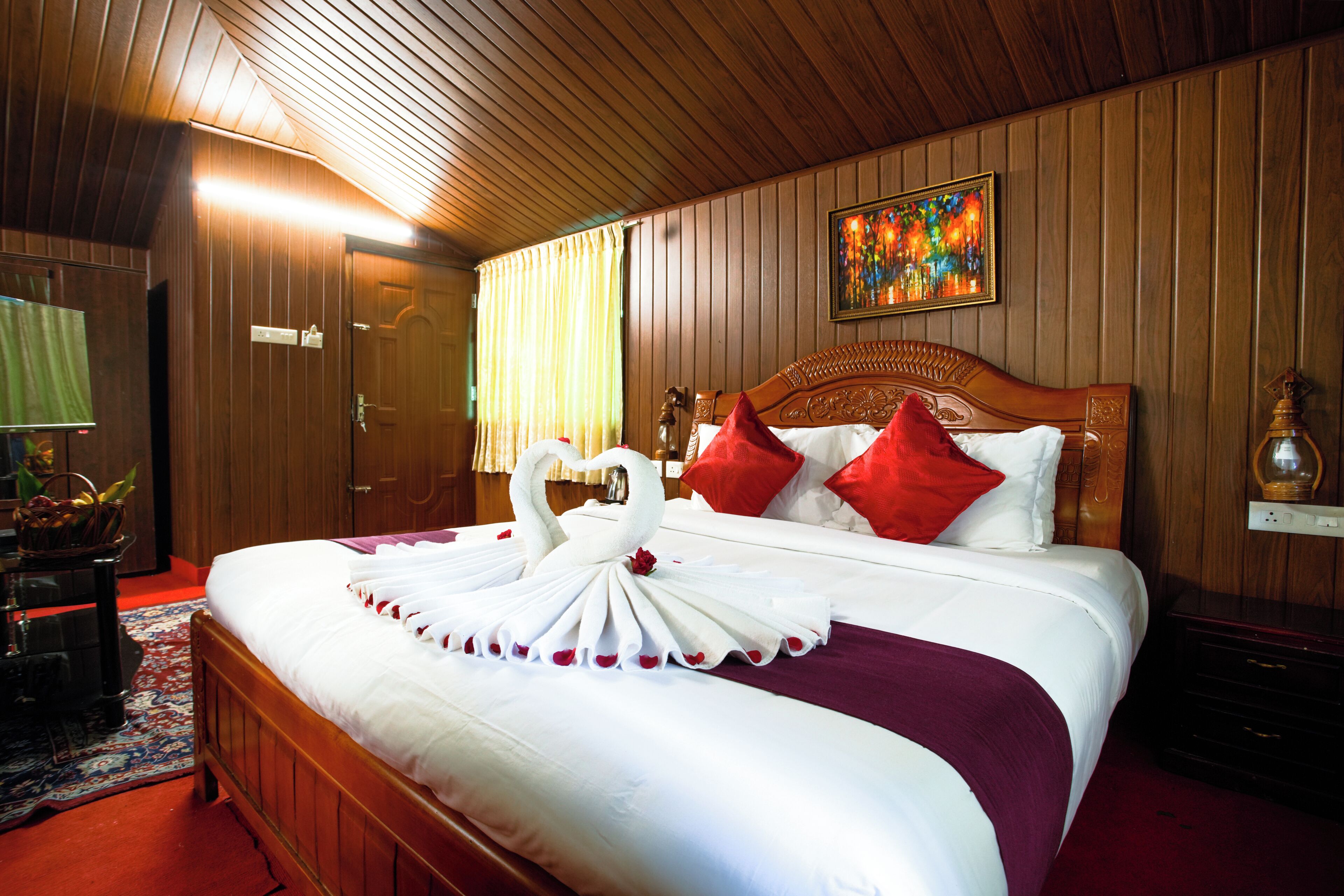 Ein Hotelzimmer mit einem hölzernen Kopfteil, einem Bett mit weißer Bettwäsche und roten Kissen, einer dekorativen Handtuch-Schwan-Arrangement, einem Bild an der Wand und einem Holzboden.