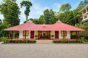 Un bâtiment à deux étages, avec un toit rouge, une entrée abritée et une allée gravillonnée.