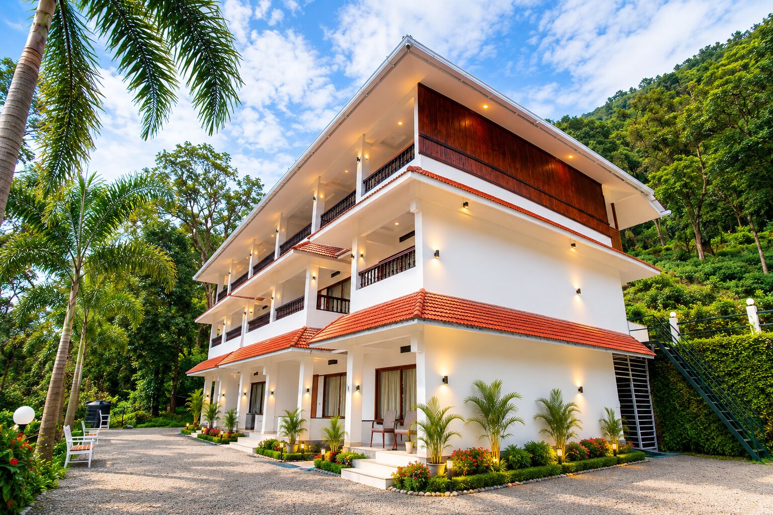A two-story building with multiple balconies, surrounded by lush greenery and a clear sky.