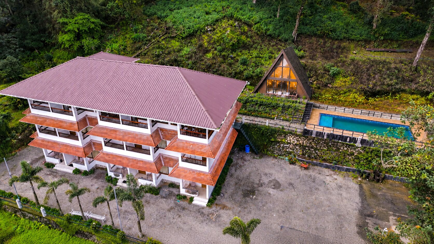 A multi-story building with a red roof, a pool, and a garden area.
