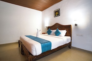 A single bed with a wooden headboard, white bedding, and blue accents. - Soma Seven Springs (Devikolam)