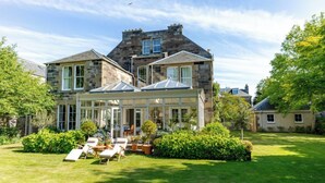 A large stone house with a conservatory, a well-maintained lawn, and outdoor seating.
