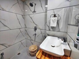 Un baño con ducha de mosaicos de mármol, un lavabo con encimera de madera y un taburete pequeño de madera.