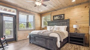Ein Schlafzimmer mit Holzbalkendecke, einem Bett mit dunklem Kopfteil, zwei Nachttischen mit Lampen und einem Schaukelstuhl.