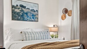Une chambre à coucher avec un lit, des oreillers, une lampe de chevet, une œuvre d’art accrochée au mur et un plaid en tissu tissé.