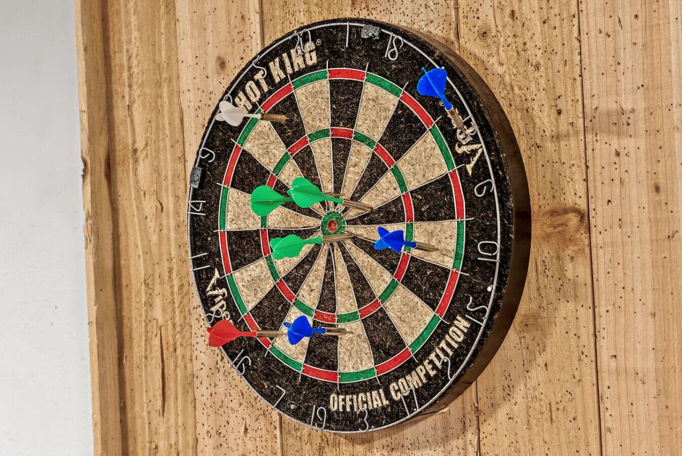 A dartboard with multiple darts stuck in it, mounted on a wooden wall.