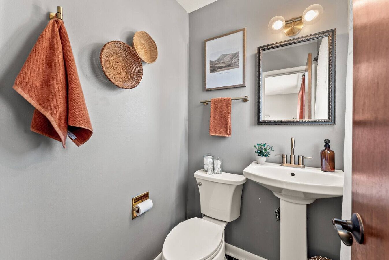 Une salle de bain avec des toilettes, un lavabo et un miroir. Des serviettes sont accrochées au mur et un tableau encadré est placé au-dessus du miroir.