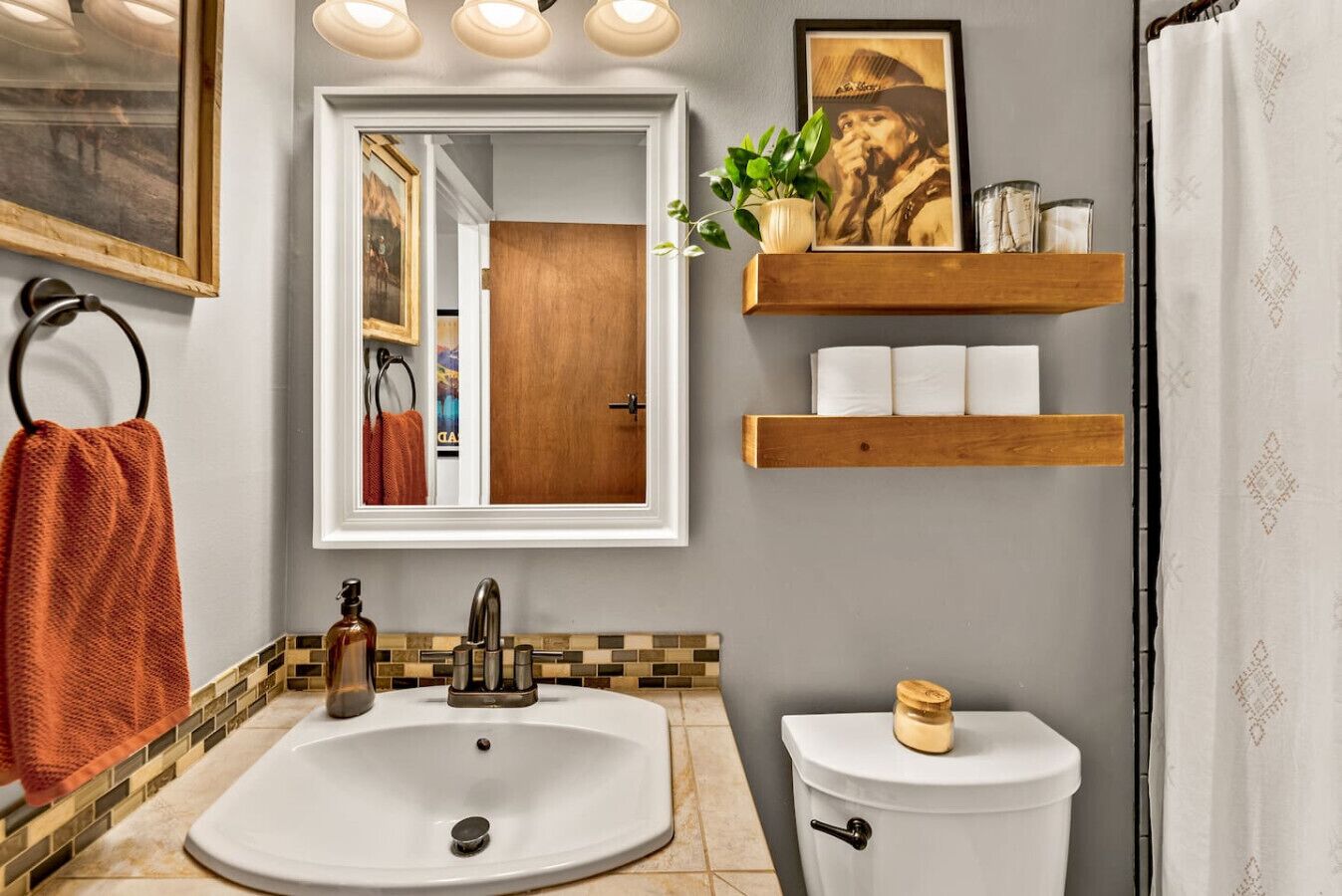 A bathroom with a white sink, a mirror, a wooden shelf with toiletries, and a toilet.