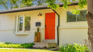 Une maison de plain-pied avec une porte rouge, une boîte aux lettres et une fenêtre avec des volets.