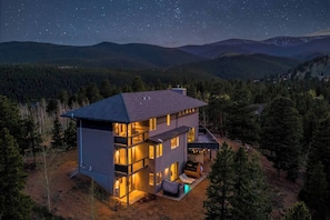 A modern two-story house with large windows, a balcony, and a well-lit outdoor area. - Summit Solace | LUXE 360° Views • Hot Tub • Games (Bailey)