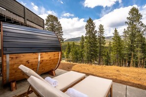 A wooden barrel, lounge chairs, and a view of a forested landscape. - Summit Solace | LUXE 360° Views • Hot Tub • Games (Bailey)
