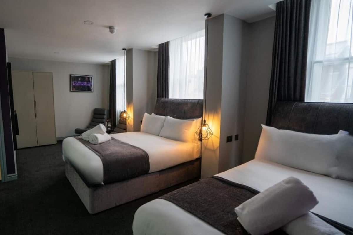 Une chambre d’hôtel avec un grand lit, un lit plus petit, un bureau et une chaise. Il y a deux tables de chevet avec des lampes.