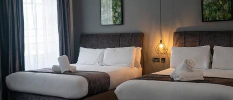 A hotel room with two beds, each with white linens and pillows, a dark headboard, and a wall-mounted light fixture.