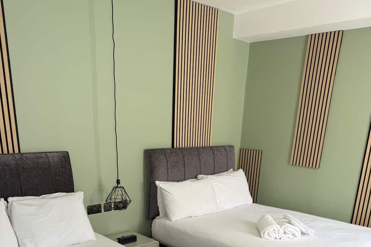 Une chambre d’hôtel avec deux lits, chacun agrémenté de draps et d’oreillers blancs, et une serviette soigneusement pliée posée sur le lit.