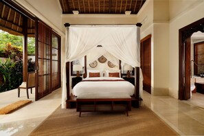 A spacious bedroom with a canopy bed, wooden headboard, and a view of lush greenery outside. - Villa Ken by Nakula (Jimbaran)