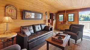 L’intérieur chaleureux d’un chalet avec un canapé en cuir, une table en bois et une vue sur l’extérieur grâce à de grandes fenêtres.