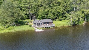 Une cabane avec un quai s’avançant dans un lac, entourée d’une forêt dense.