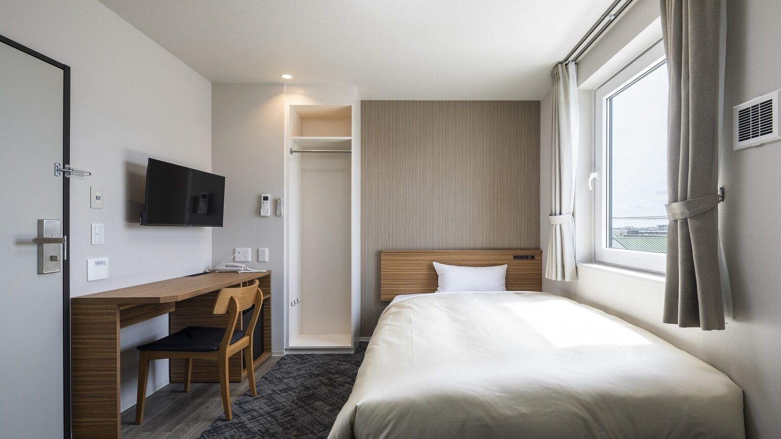 Habitación de hotel con cama, escritorio, silla, televisor, ventana y armario.