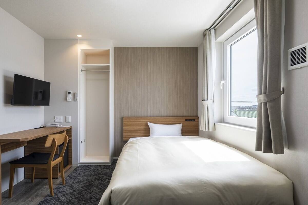 A hotel room with a bed, a desk, a chair, a television, a window, and a closet.