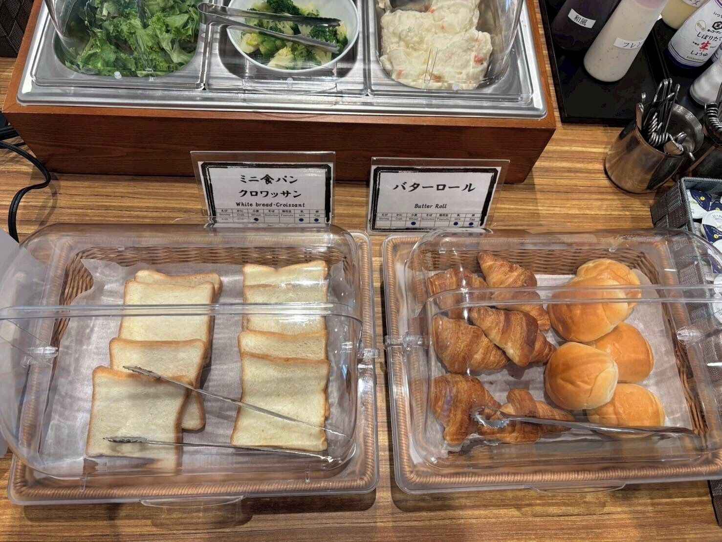 A buffet with labeled food items including bread, croissants, and a salad.