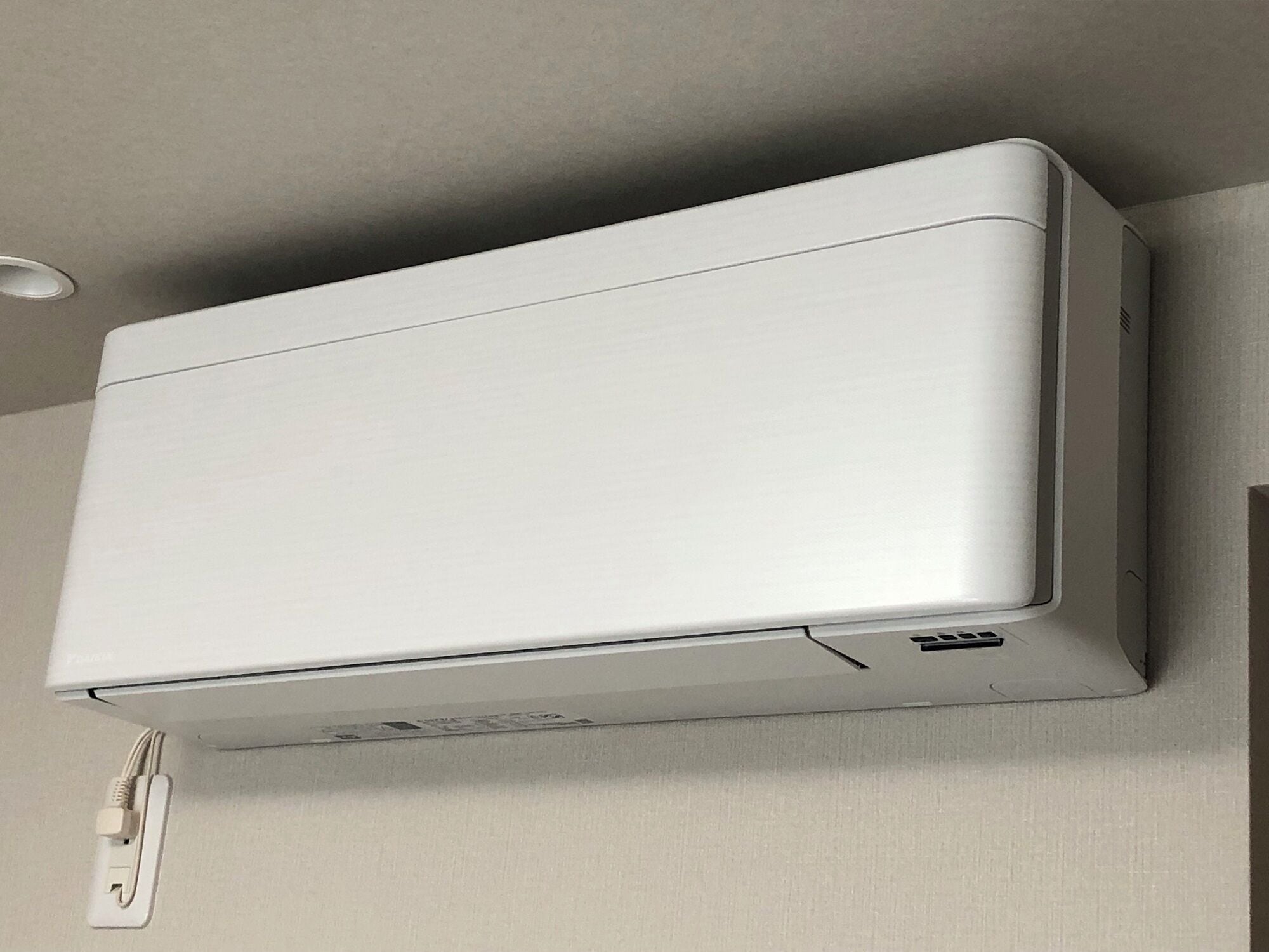 A white air conditioning unit mounted on a wall with a power outlet below it.