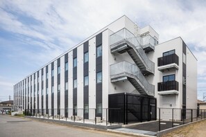 A modern building with a white facade, multiple windows, and a black metal staircase leading to an upper level. - Hotel Crown Hills Goi (Ichihara)