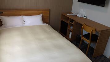 A hotel room with a bed, a wooden desk, a chair, and a flat-screen TV mounted on the wall.