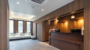 Un área de recepción moderna con un mostrador de madera, un espacio de descanso con un banco y grandes ventanales que dejan entrar luz natural.