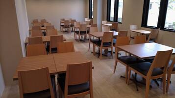 A spacious dining area with multiple wooden tables and chairs, large windows providing natural light, and a clean, modern interior design.