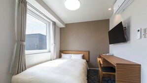 Habitación de hotel con cama, escritorio, silla, televisor y ventana con cortinas.