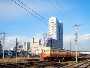 A train on tracks with a large building in the background. - Hotel Crown Hills Goi (Ichihara)
