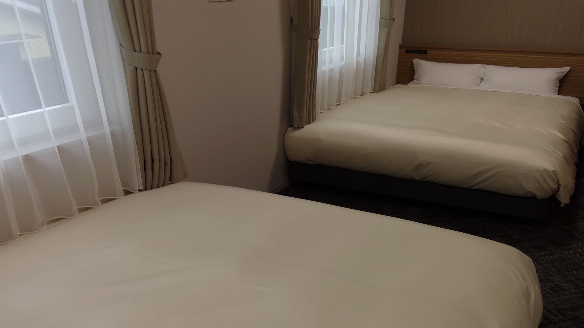 Habitación de hotel con dos camas, cabecero de madera y cortinas translúcidas.